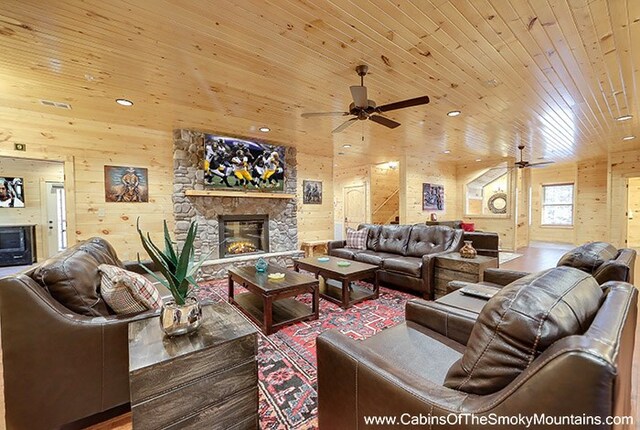 living room featuring a stone fireplace, ceiling fan, wooden walls, and wood ceiling