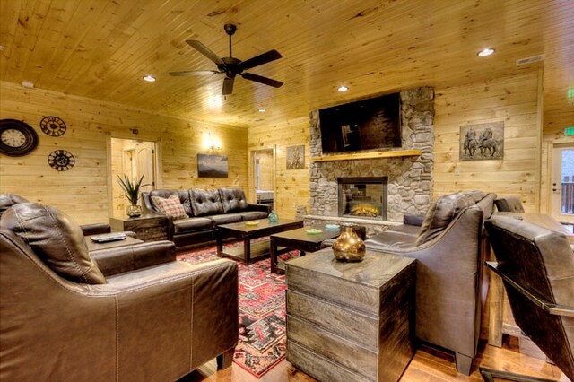 living room featuring wood walls, wooden ceiling, light hardwood / wood-style flooring, ceiling fan, and a fireplace