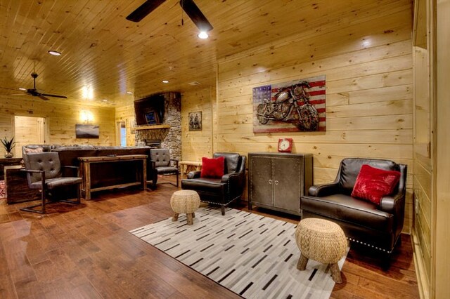sitting room with hardwood / wood-style floors, wooden walls, ceiling fan, a fireplace, and wood ceiling