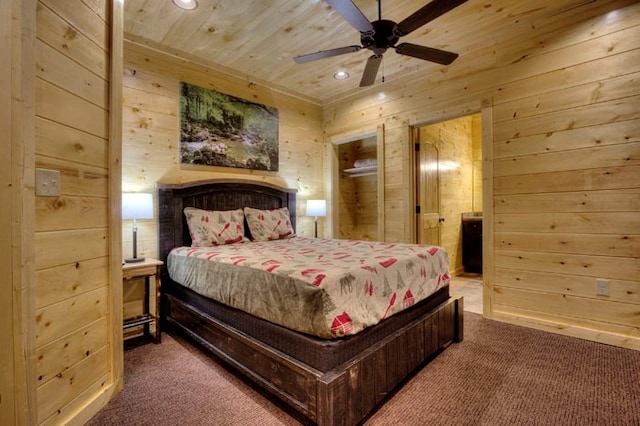 bedroom with carpet flooring, ceiling fan, wood walls, and ensuite bath