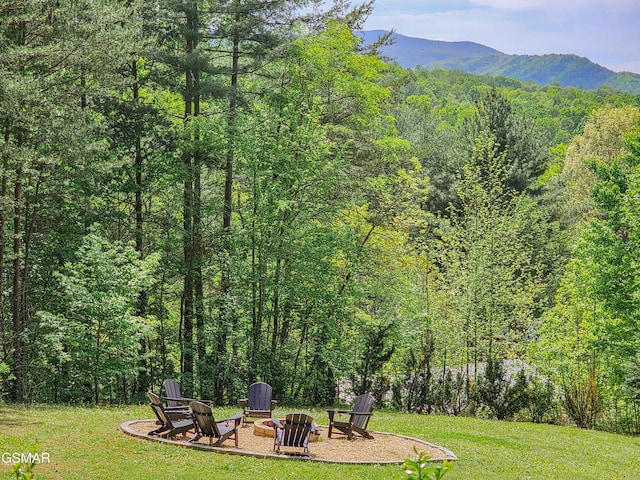 view of yard featuring a mountain view, an outdoor fire pit, and a wooded view