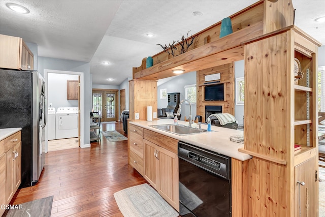 kitchen featuring stainless steel refrigerator with ice dispenser, wood finished floors, dishwasher, a sink, and washer and dryer