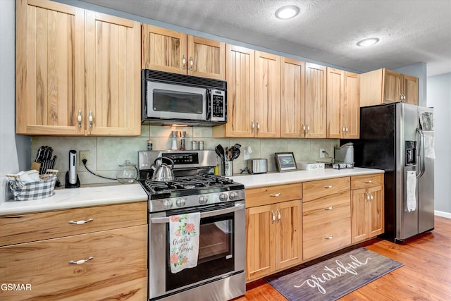 kitchen featuring light countertops, appliances with stainless steel finishes, tasteful backsplash, and light wood-style floors