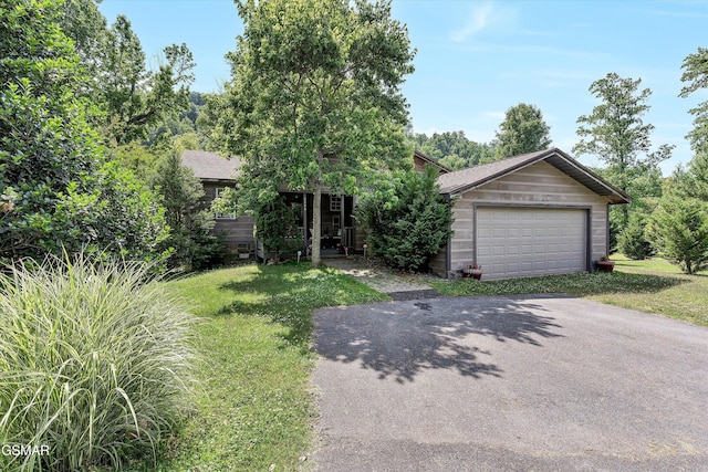 obstructed view of property featuring a detached garage, a front yard, and aphalt driveway