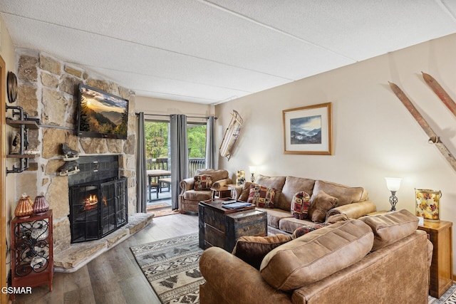 living room featuring hardwood / wood-style flooring, a stone fireplace, and a textured ceiling