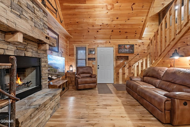 living room featuring wood ceiling, wooden walls, high vaulted ceiling, light hardwood / wood-style floors, and a stone fireplace