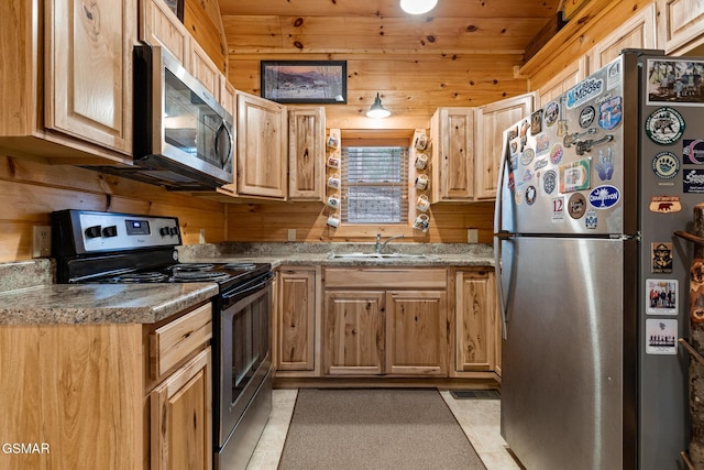 kitchen featuring sink, light tile patterned floors, stainless steel appliances, and wooden walls