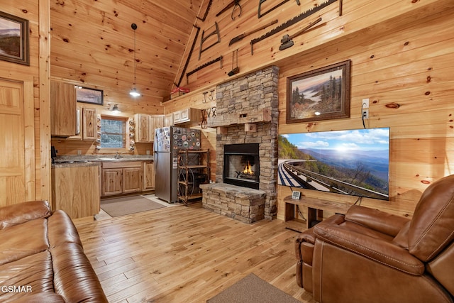 living room with wooden walls, a stone fireplace, light wood-type flooring, and high vaulted ceiling