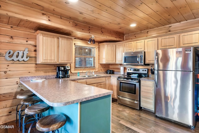 kitchen with a kitchen bar, sink, wood walls, light brown cabinets, and appliances with stainless steel finishes