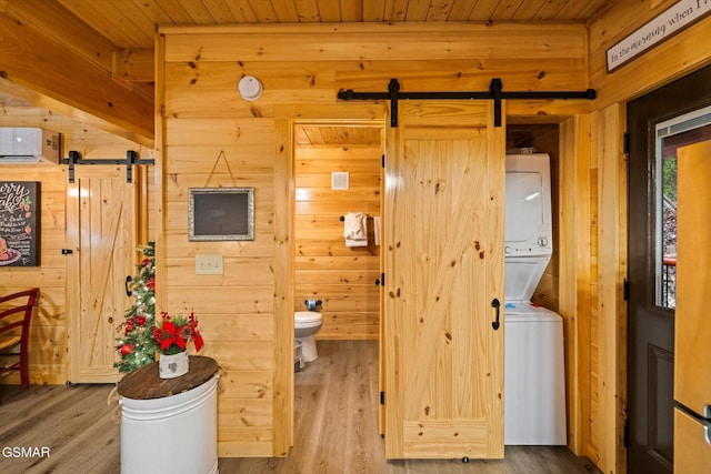 bathroom with hardwood / wood-style floors, stacked washer / drying machine, toilet, and wooden walls