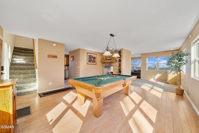 recreation room with a stone fireplace, billiards, and light wood-type flooring