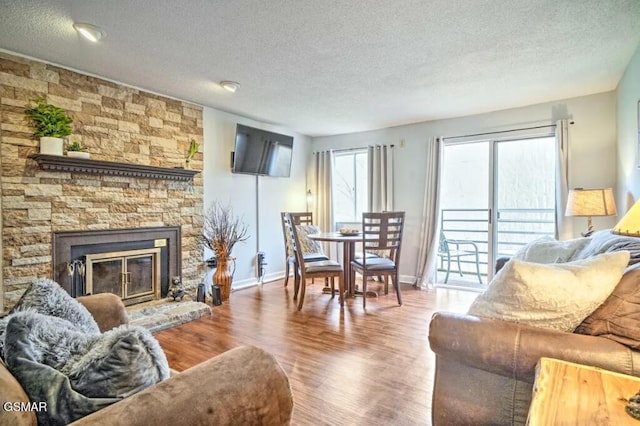 living room with a textured ceiling, a stone fireplace, wood finished floors, and baseboards