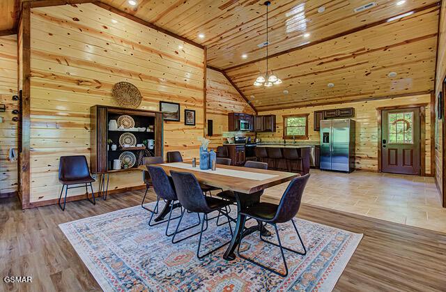 dining room featuring wood walls, high vaulted ceiling, light hardwood / wood-style flooring, a notable chandelier, and wood ceiling