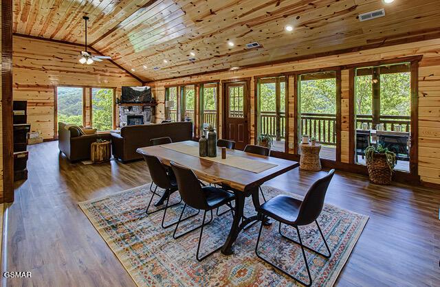 dining area featuring a stone fireplace, wood walls, and wood ceiling