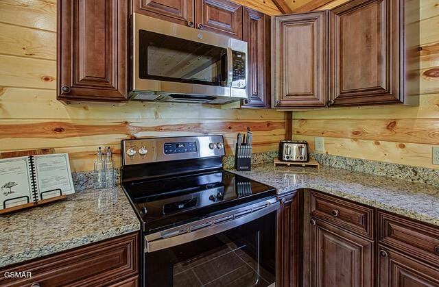 kitchen featuring wood walls, light stone countertops, and stainless steel appliances