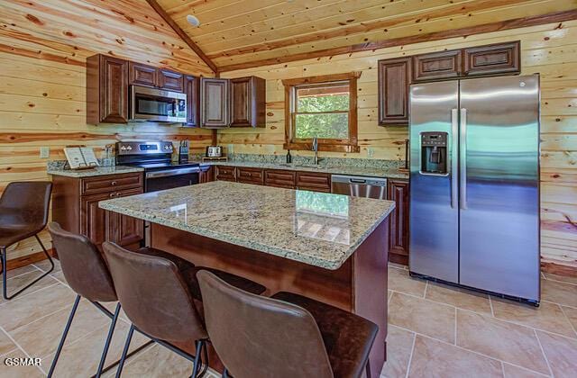 kitchen with appliances with stainless steel finishes, vaulted ceiling, wooden walls, wooden ceiling, and a kitchen island