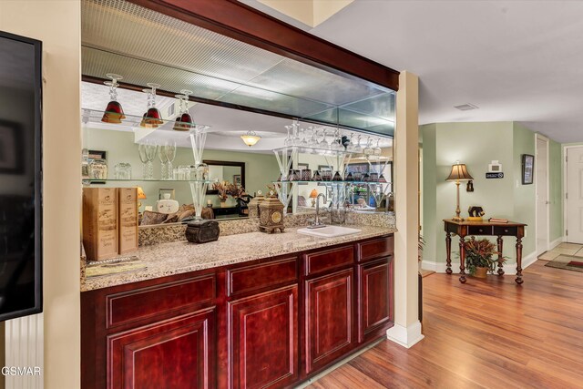 bar featuring light stone countertops, sink, and light wood-type flooring