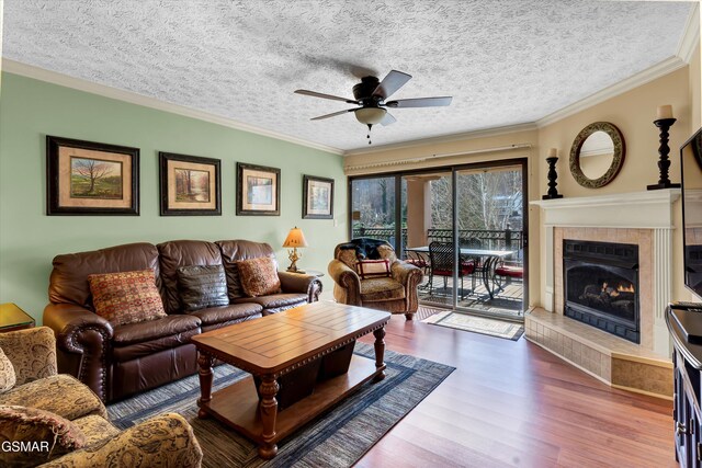 living room featuring ornamental molding, a textured ceiling, ceiling fan, hardwood / wood-style flooring, and a fireplace