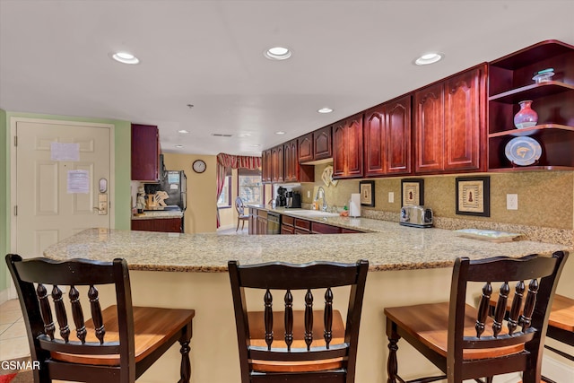 kitchen featuring light stone countertops, sink, tasteful backsplash, kitchen peninsula, and light tile patterned floors