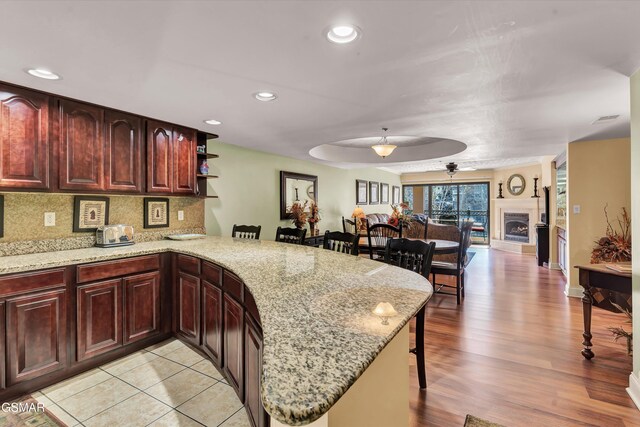 kitchen with ceiling fan, light wood-type flooring, tasteful backsplash, light stone counters, and kitchen peninsula