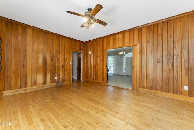 empty room with wood walls, light hardwood / wood-style flooring, and ceiling fan with notable chandelier