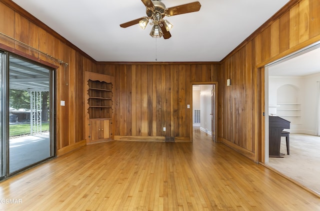 empty room featuring light hardwood / wood-style flooring, ceiling fan, crown molding, and wood walls