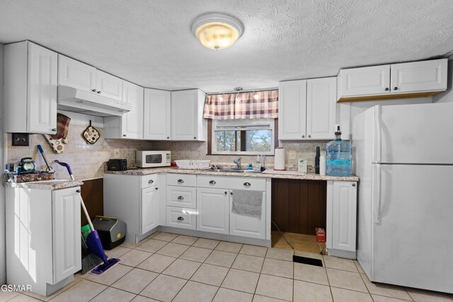 kitchen featuring sink, white cabinets, a textured ceiling, white appliances, and light tile patterned floors