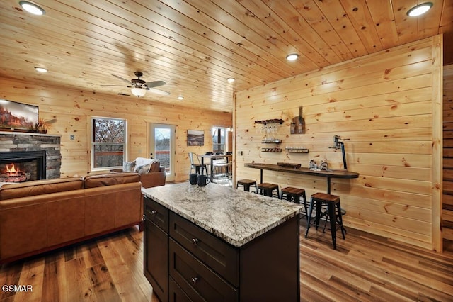 kitchen with light stone countertops, dark brown cabinets, ceiling fan, light hardwood / wood-style flooring, and wood walls