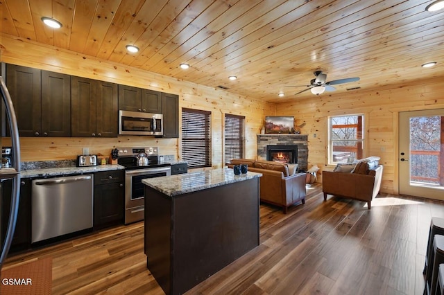 kitchen featuring dark brown cabinetry, a center island, stainless steel appliances, light stone counters, and a fireplace