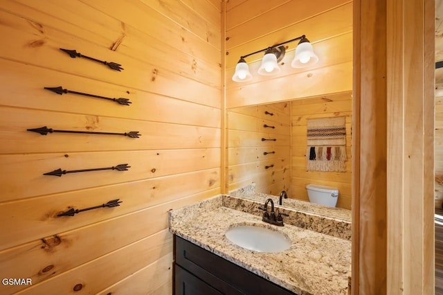 bathroom featuring vanity, toilet, and wooden walls