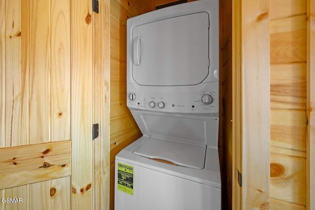 clothes washing area with wood walls and stacked washing maching and dryer