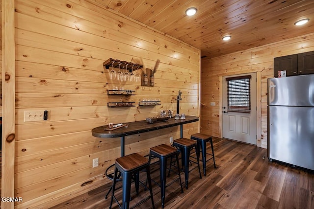 bar featuring stainless steel refrigerator, wooden walls, dark wood-type flooring, and wooden ceiling