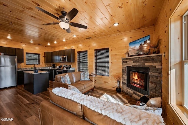 living room with a stone fireplace, ceiling fan, dark hardwood / wood-style flooring, and wooden walls