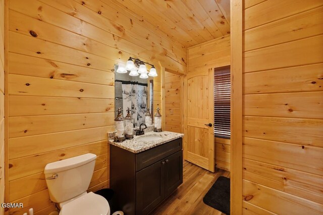 bathroom with vanity, toilet, wood-type flooring, and wooden walls