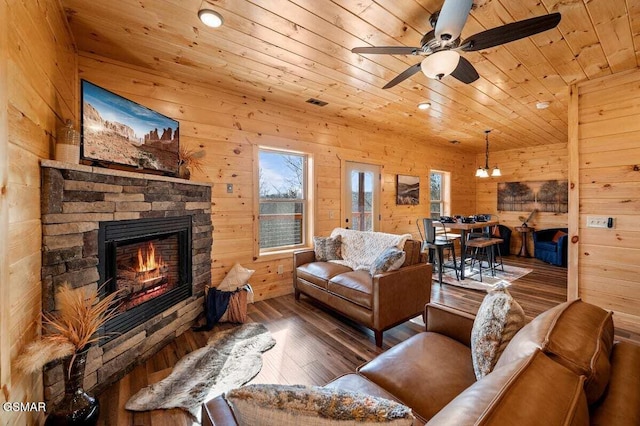 living room with a stone fireplace, wood walls, hardwood / wood-style floors, wood ceiling, and ceiling fan with notable chandelier