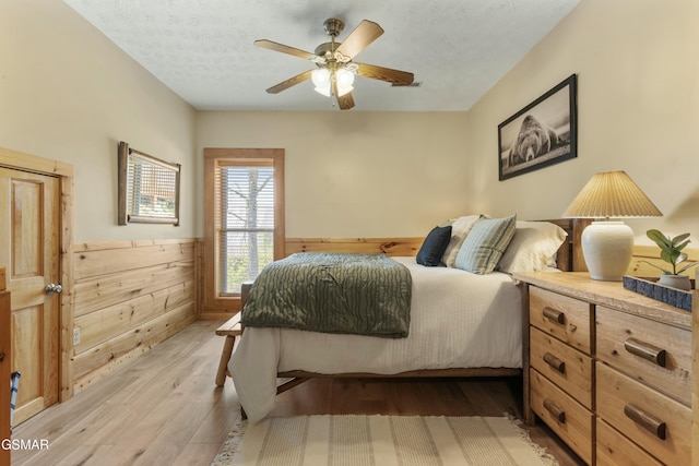 2851 Indigo Ln, Sevierville, TN 37862 - bedroom featuring a textured ceiling, light wood-type flooring, wainscoting, ceiling fan, and wooden walls