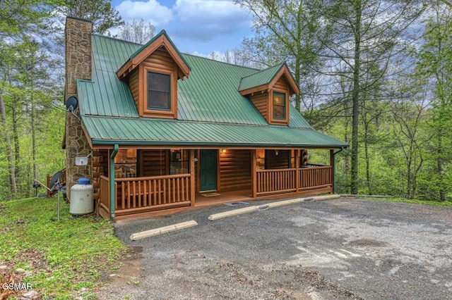 view of front of property with metal roof, uncovered parking, covered porch, and a chimney