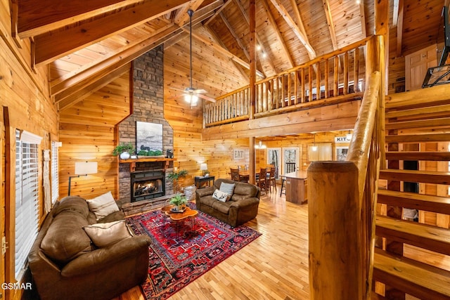 living room featuring a stone fireplace, wood walls, stairway, and wood ceiling