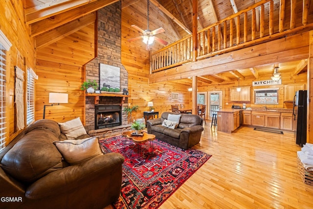 living room with vaulted ceiling with beams, a stone fireplace, light wood-style floors, wood walls, and wooden ceiling