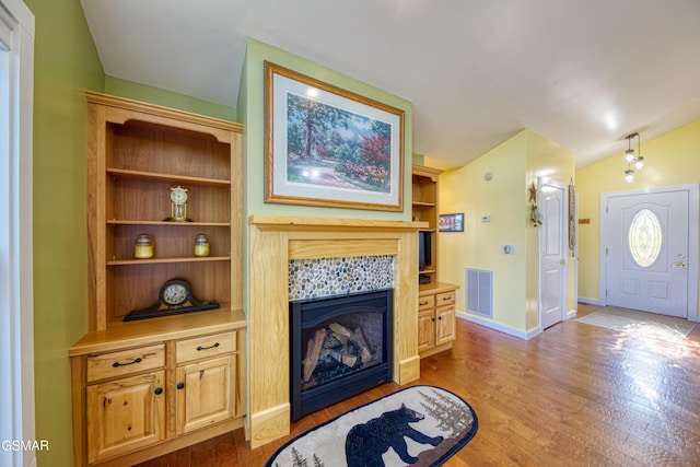 living room featuring baseboards, visible vents, a tiled fireplace, wood finished floors, and vaulted ceiling