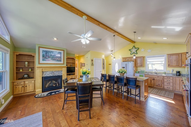 dining room featuring vaulted ceiling with beams, ceiling fan, a fireplace, and dark wood finished floors