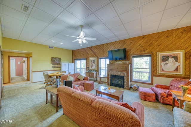 living room with light carpet, a glass covered fireplace, visible vents, and wooden walls