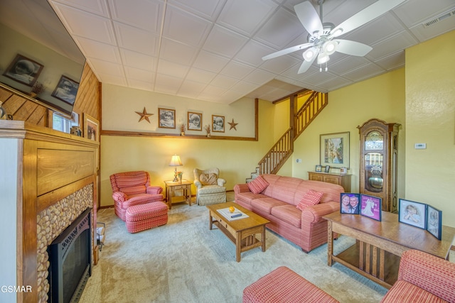 living room featuring a fireplace, light colored carpet, visible vents, ceiling fan, and stairs