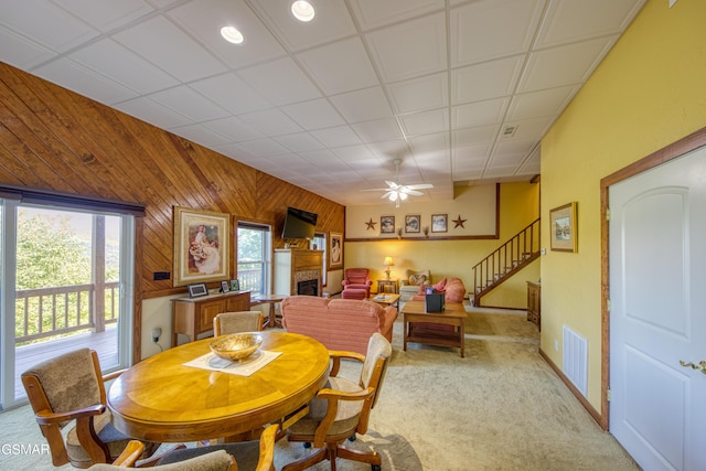 dining area featuring a fireplace, light colored carpet, visible vents, wood walls, and stairs