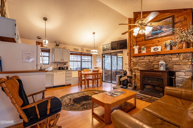 living room with ceiling fan, light wood-type flooring, a fireplace, and high vaulted ceiling