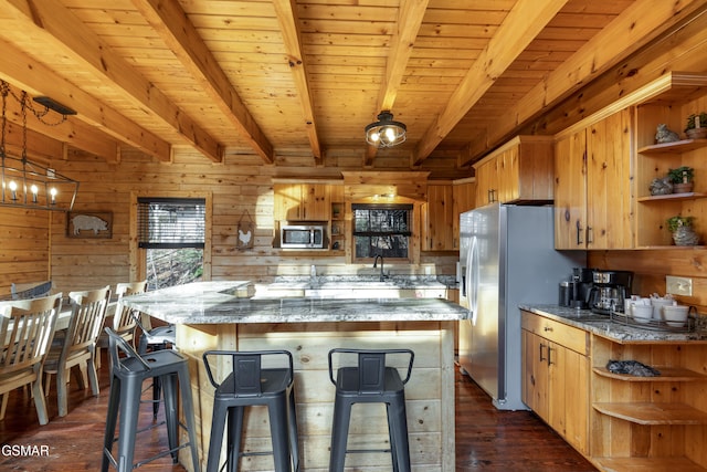 kitchen featuring beam ceiling, stainless steel appliances, wooden walls, and a breakfast bar area