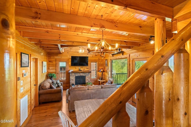 living room featuring beamed ceiling, a fireplace, wooden walls, and an inviting chandelier