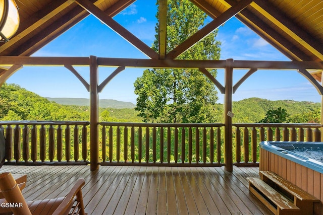 wooden deck featuring a mountain view, a hot tub, and a forest view