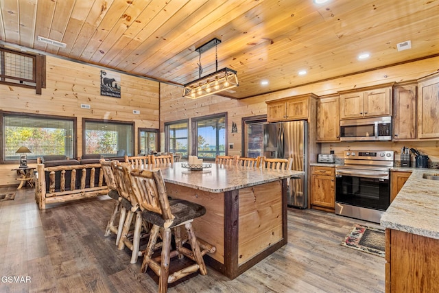 kitchen featuring stainless steel appliances, dark hardwood / wood-style floors, wood walls, decorative light fixtures, and wood ceiling