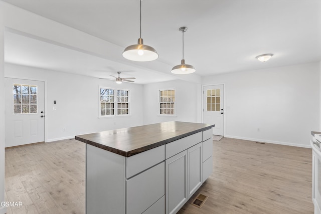 kitchen featuring light wood finished floors, butcher block counters, visible vents, plenty of natural light, and baseboards